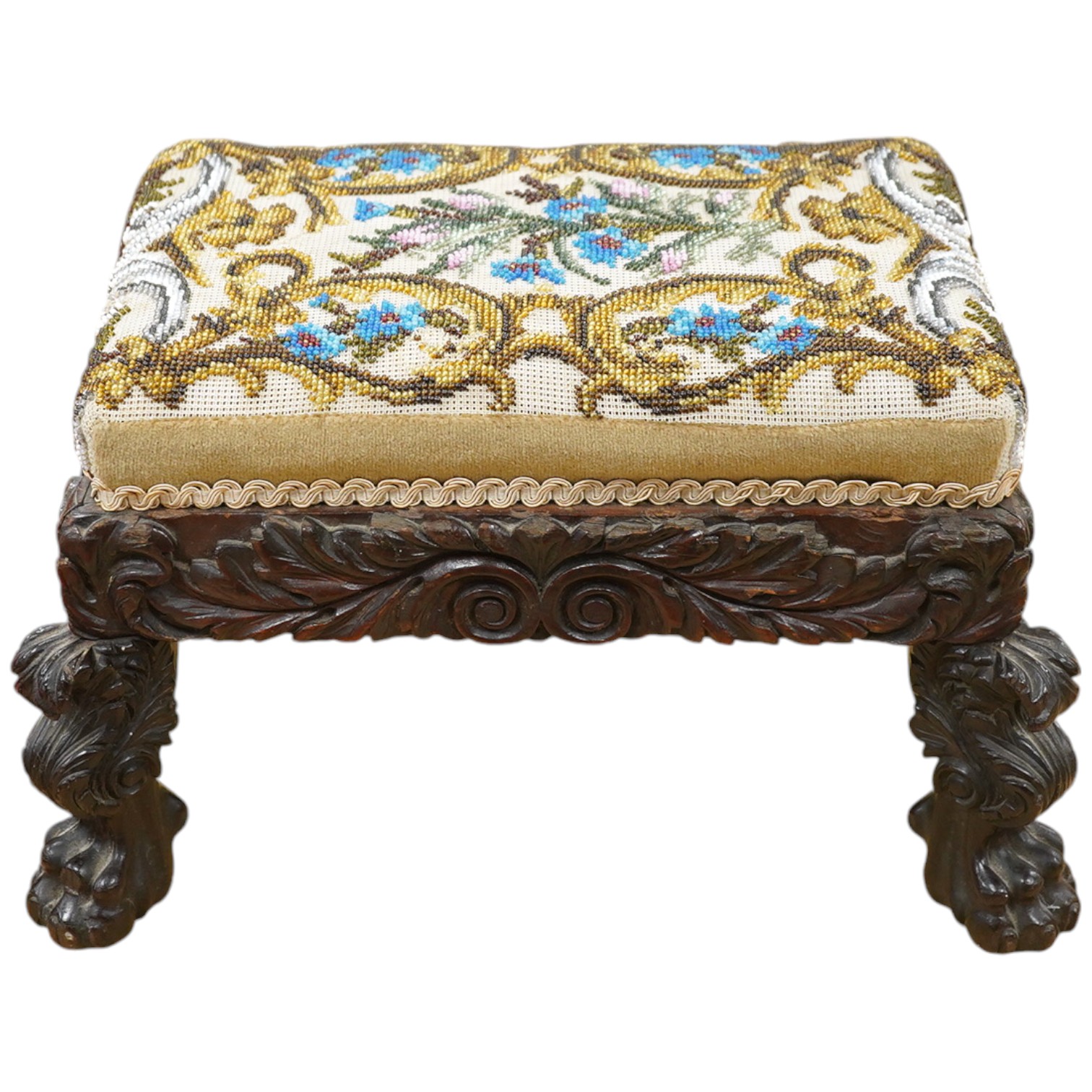 A 19th century ornately carved paw foot, Berlin beadwork upholstered footstool, the bead work a scrolling multi-coloured floral pattern, upholstered into a heavily carved frame and legs on carved paw feet, beadwork 21cm